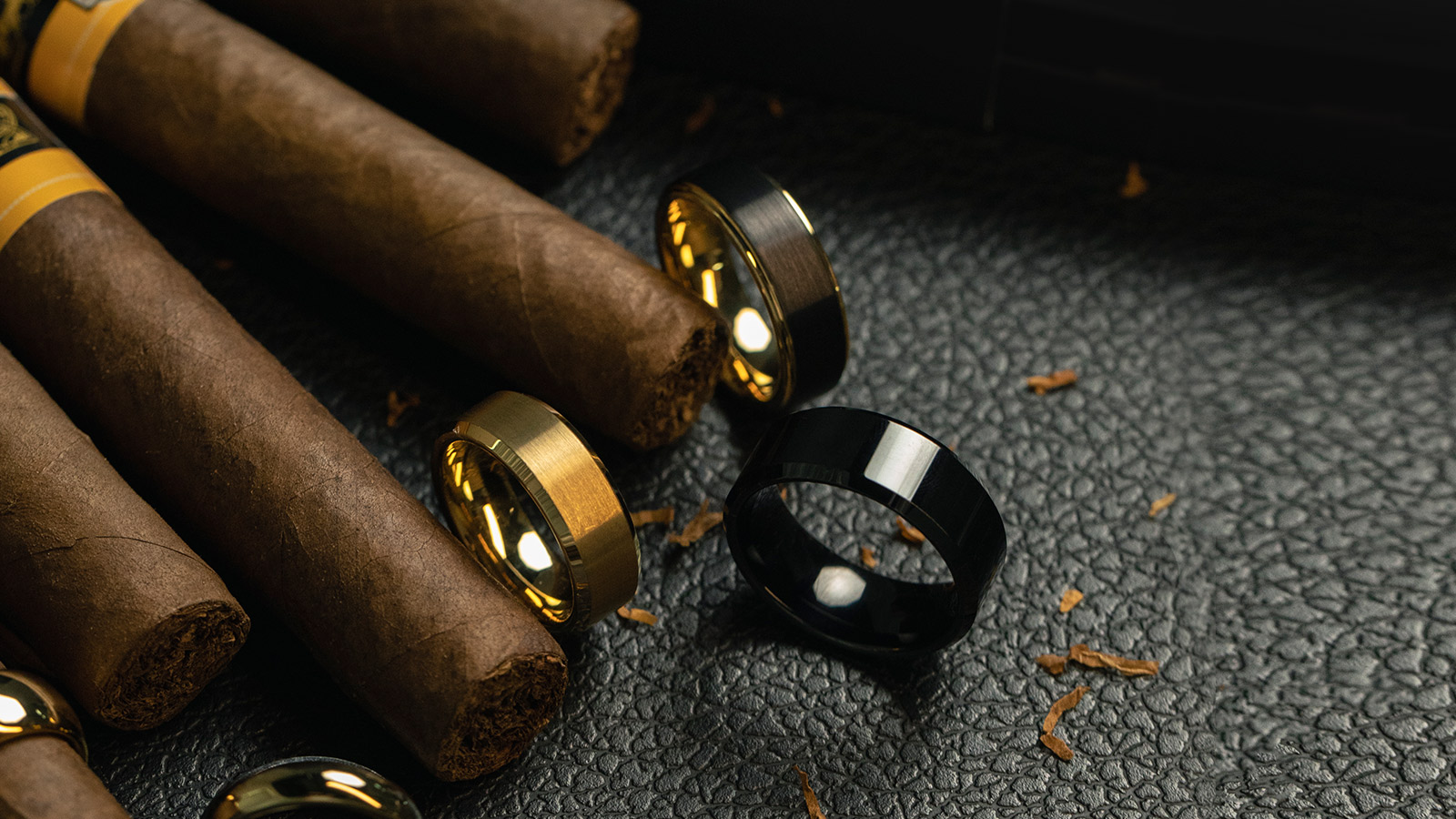 Three tungsten wedding rings were placed on leather, next to cigars