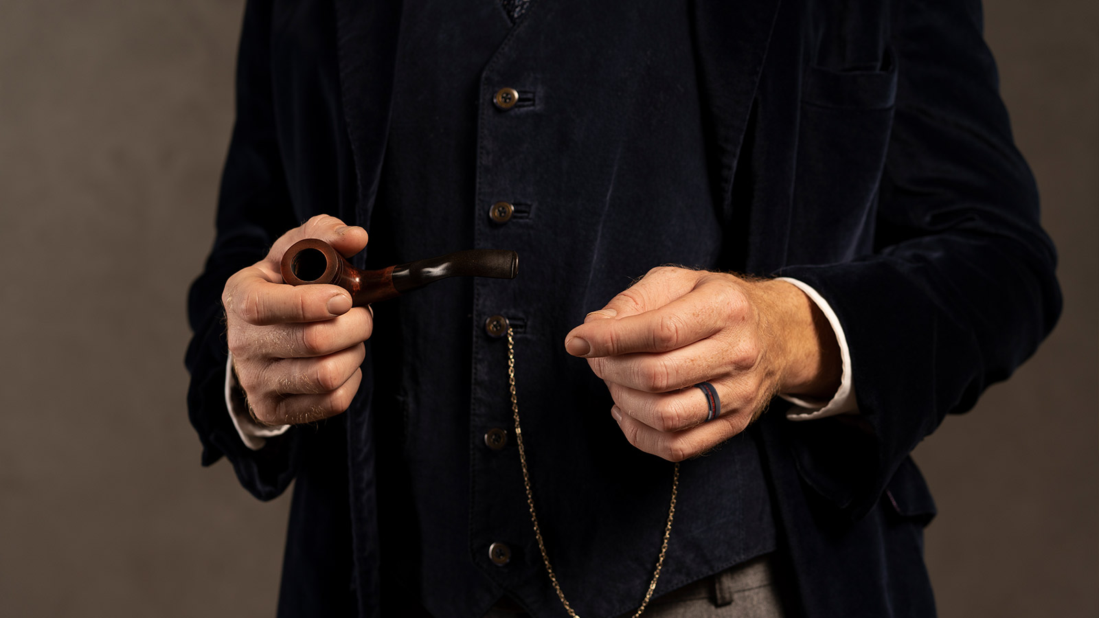 The man holds a cigarette pipe in his right hand and a men's ring in his left