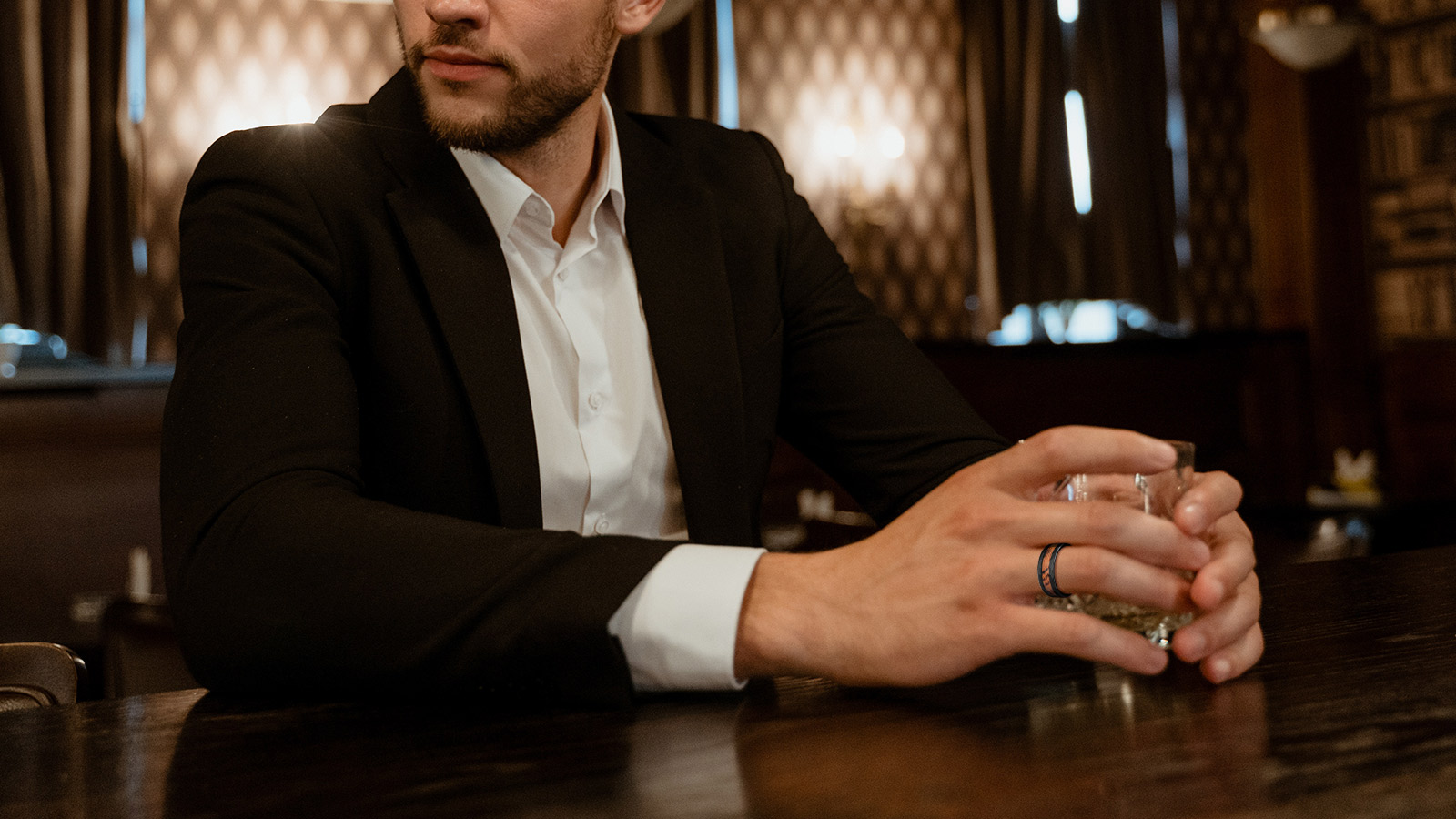 A man sitting at the bar with a glass of wine and a man's ring on his finger