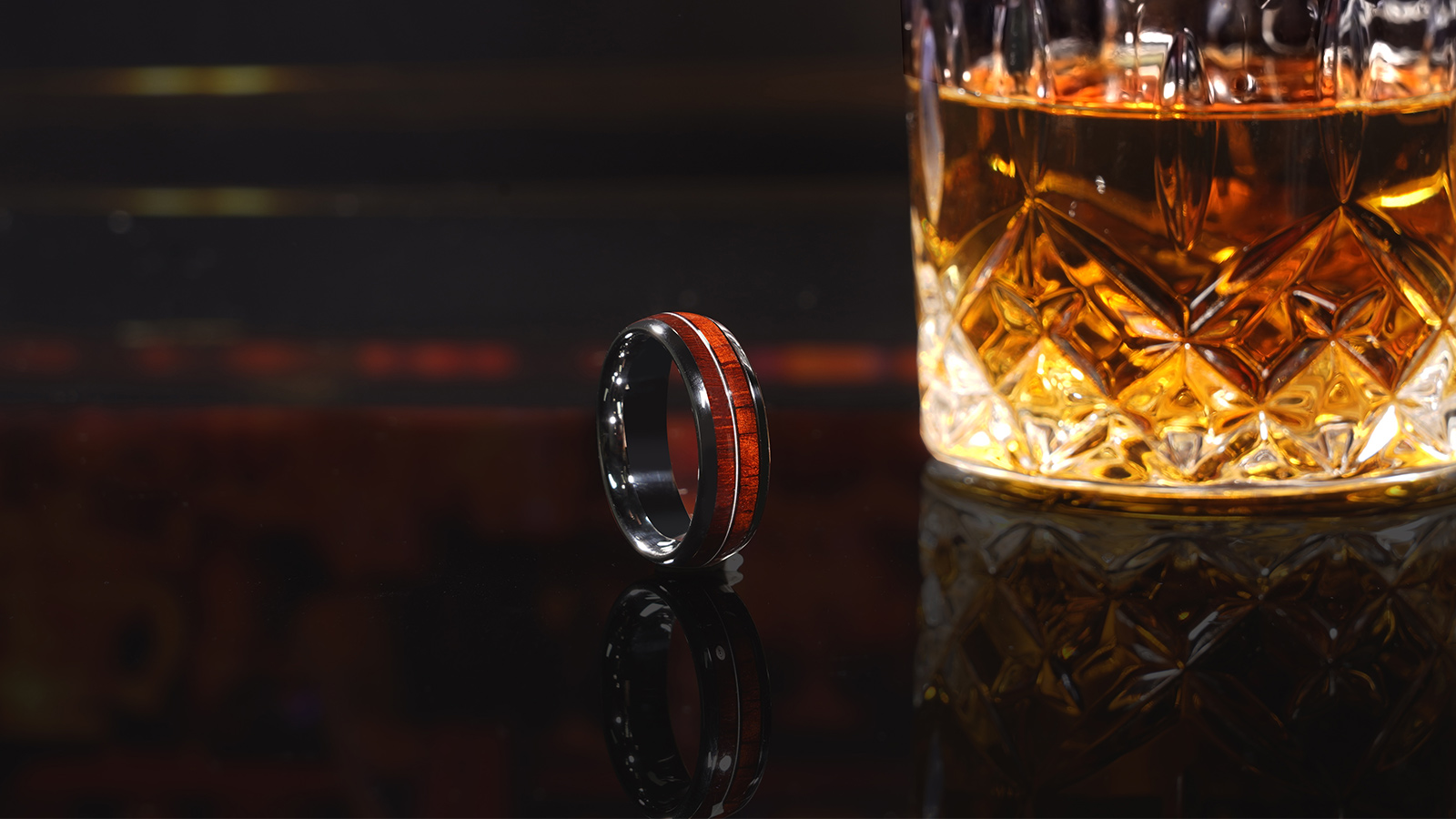 A black men's ring with a wooden setting and a glass of beer next to it